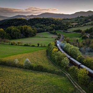 Scenic aerial view of a vintage train traveling through lush green countryside with rolling hills at sunset.