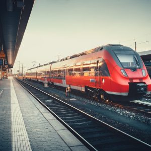 Beautiful railway station with modern red commuter train at colorful sunset in Nuremberg, Germany. Railroad with vintage toning